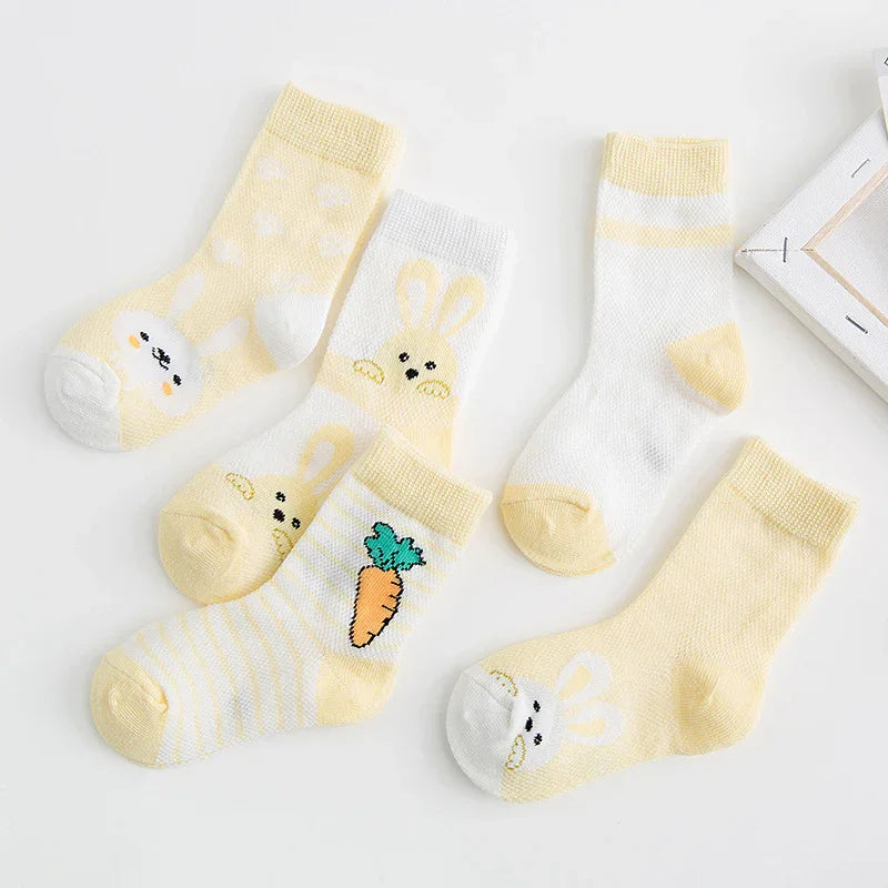 Five pairs of pastel yellow and white baby socks with bunny and carrot designs on white background