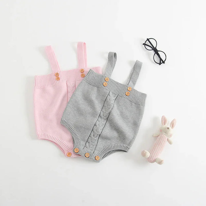 Soft pink and gray knitted baby rompers with button details, black glasses, and a plush bunny toy
