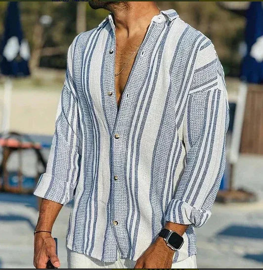 Man wearing casual blue and white striped button-up long sleeve shirt with rolled cuffs at outdoor beach setting