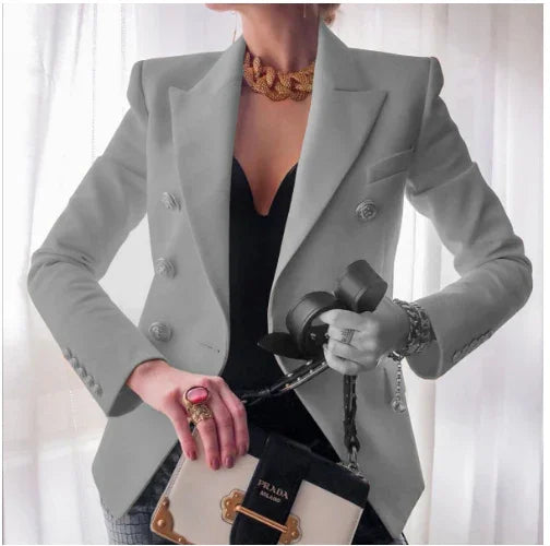 Woman wearing double-breasted gray blazer, black top, chunky gold necklace, holding Prada handbag and camera