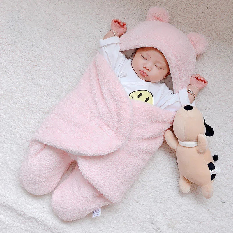 Sleeping baby wrapped in soft pink bear hooded blanket with plush toy on white textured blanket