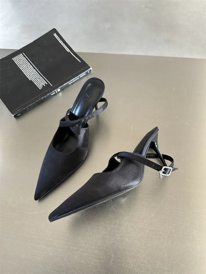 Pair of black pointed-toe slingback high heels with buckle strap on beige surface next to black book