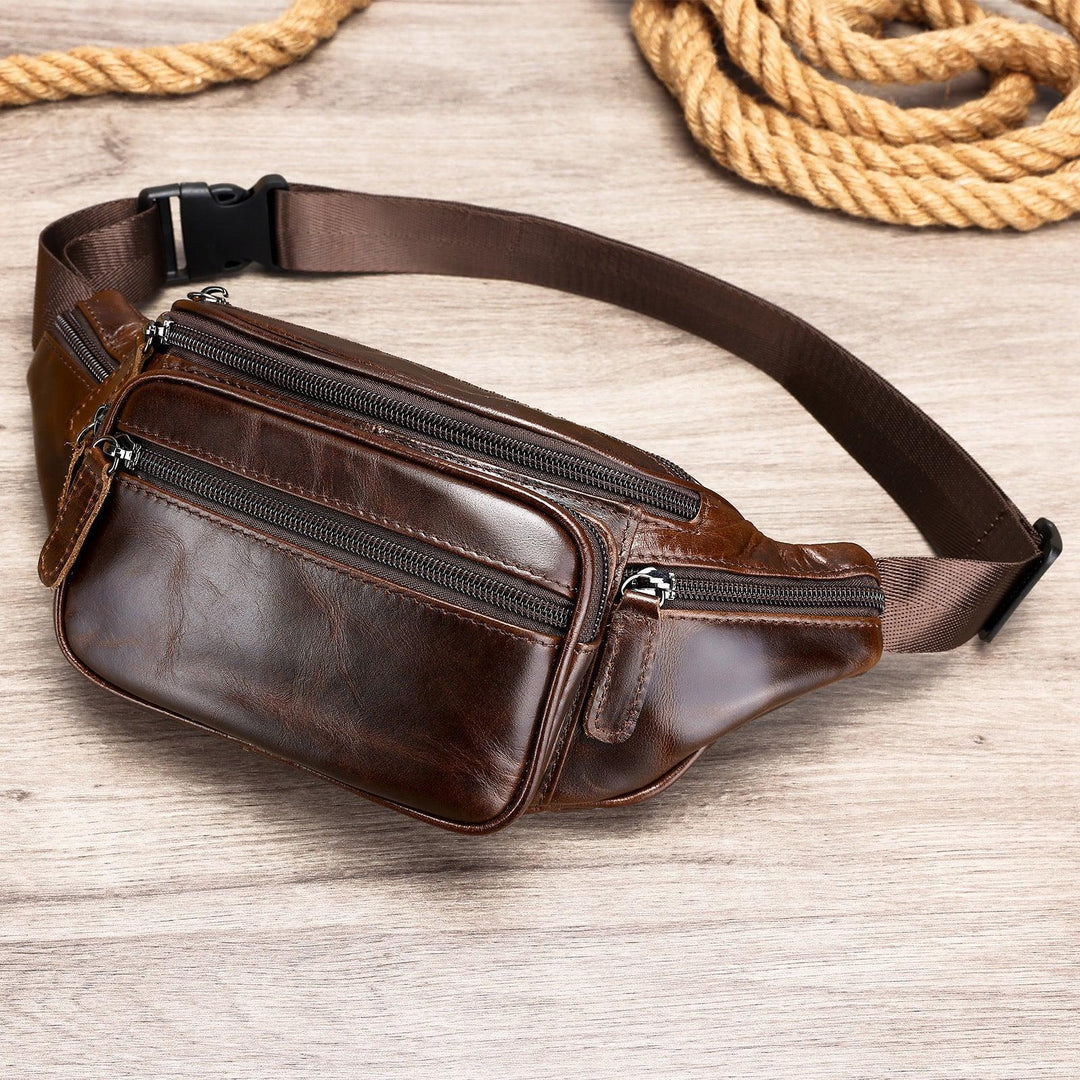 dark brown leather waist bag with multiple zippered compartments on wooden surface