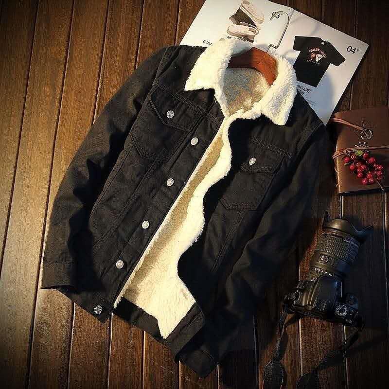 Black denim jacket with white sherpa lining displayed on wooden floor with camera and magazine