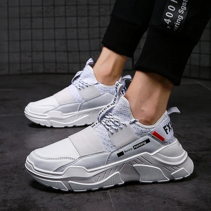 White and gray chunky athletic sneakers with 'keep running' text worn with black pants on dark tile floor
