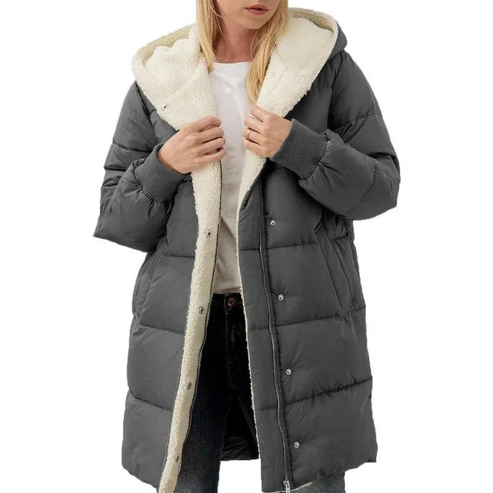 Woman wearing a long dark gray puffer coat with white fleece lining and hood over casual white top and jeans