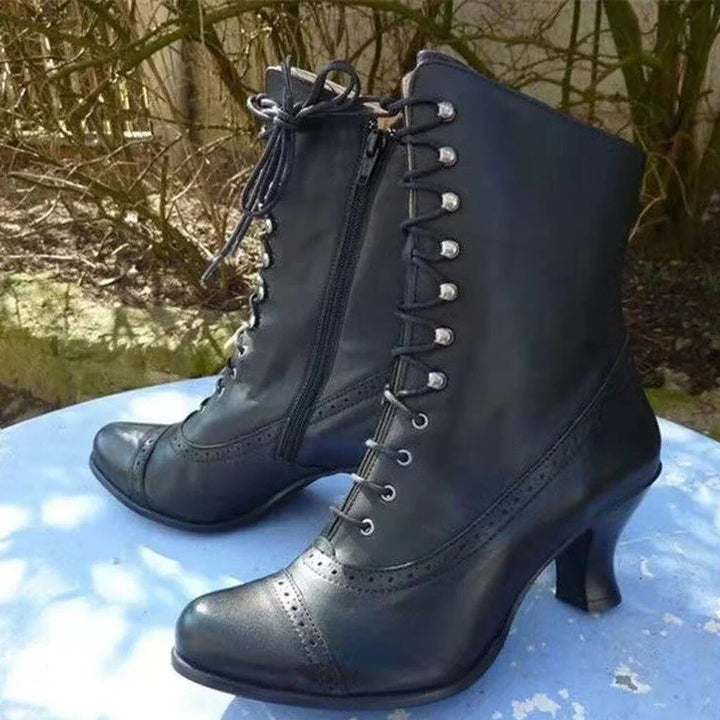 Pair of black vintage leather lace-up mid-heel boots on blue surface with outdoor background