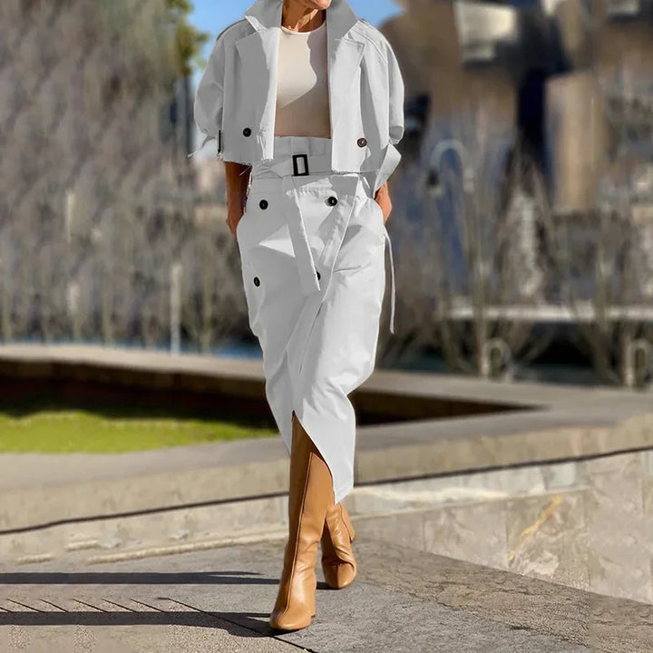 Woman in white crop trench coat and high-waisted belted skirt with tan knee-high boots outdoors