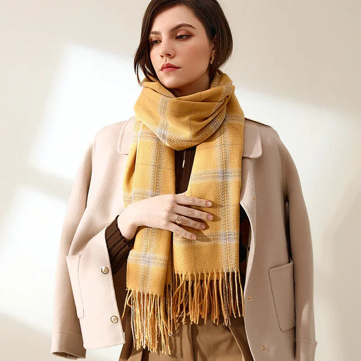 Woman wearing beige coat and mustard yellow plaid scarf with fringe in soft natural light