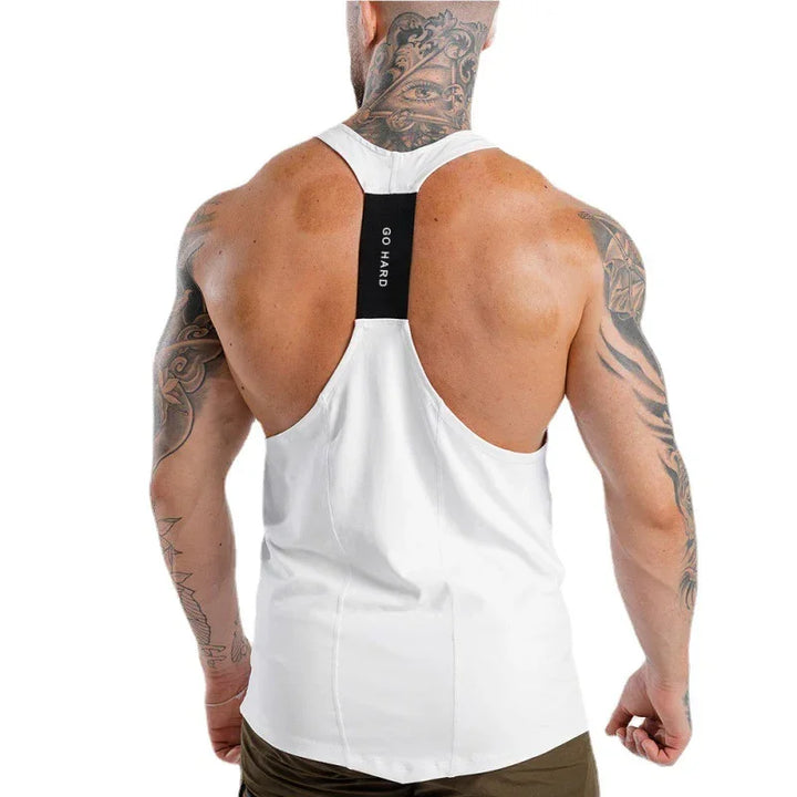 Muscular man with tattoos wearing white gym tank top with black strap and 'GO HARD' text on back