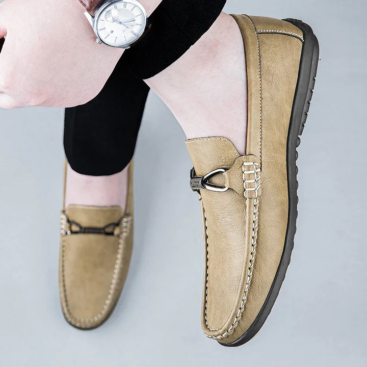 Beige leather men's loafers with metal buckle detail, worn with black pants and silver watch