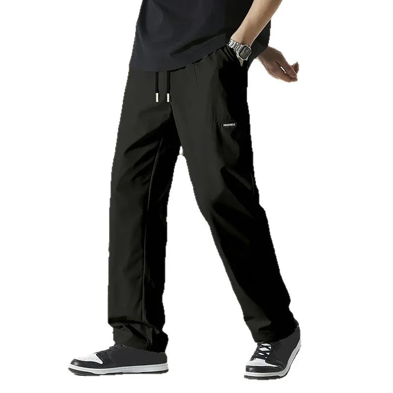 Man wearing black casual pants with drawstring and sneakers, mid-walk pose on white background