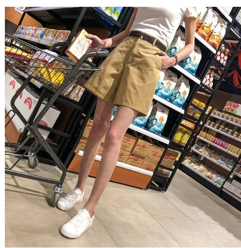 person wearing beige shorts, white sneakers, and white top shopping with cart in grocery store aisle