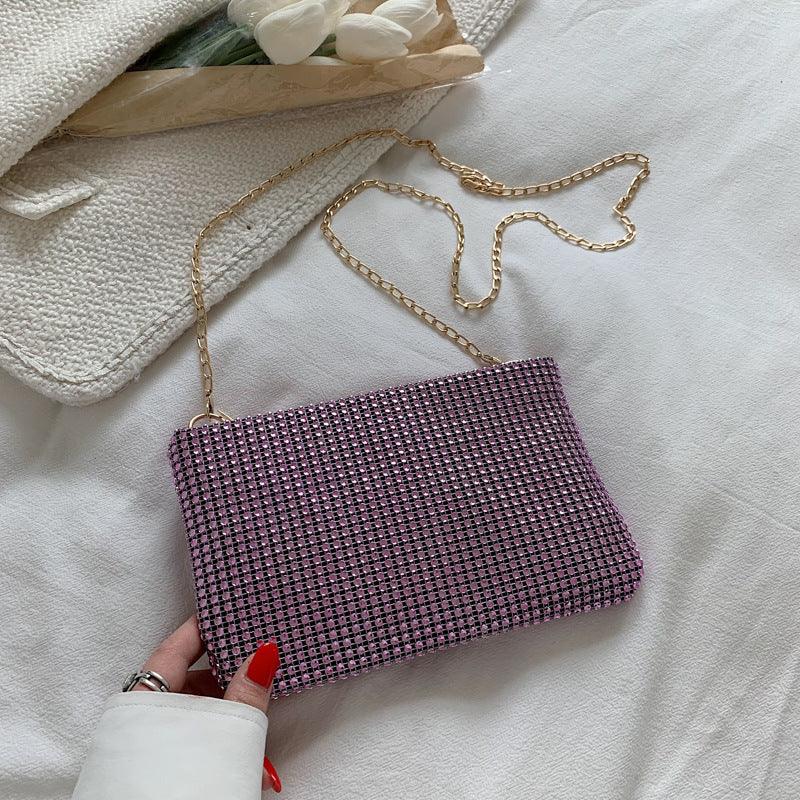 Purple beaded clutch bag with gold chain strap on white fabric, hand with red nails holding it