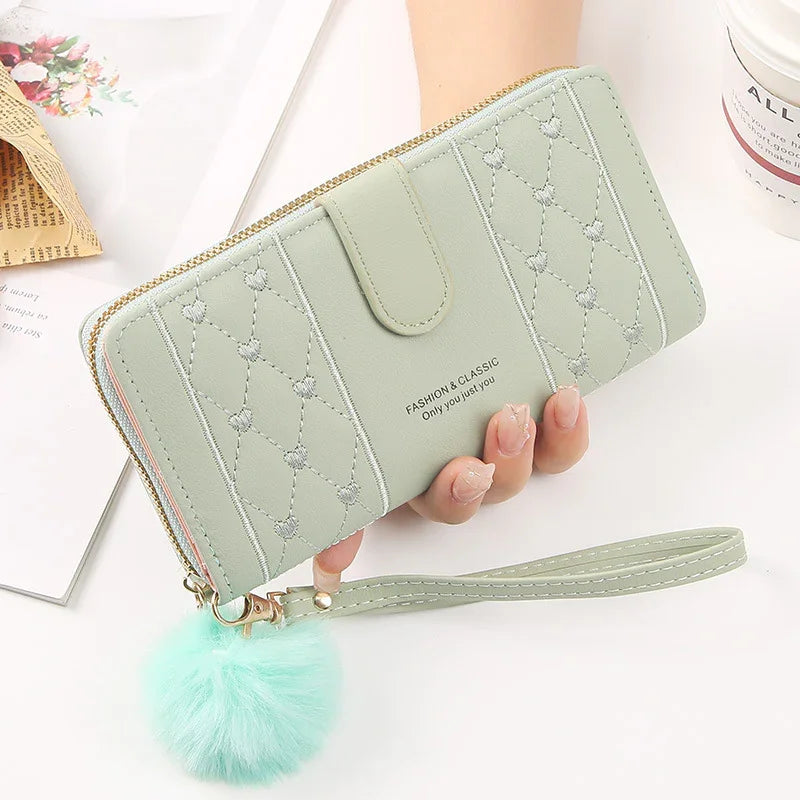 Light green quilted wallet with heart stitching, wrist strap, and fluffy pom-pom keychain