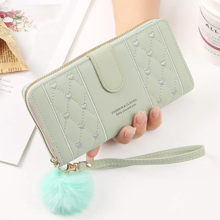 Light green quilted wallet with heart stitching, wrist strap, and fluffy pom-pom keychain