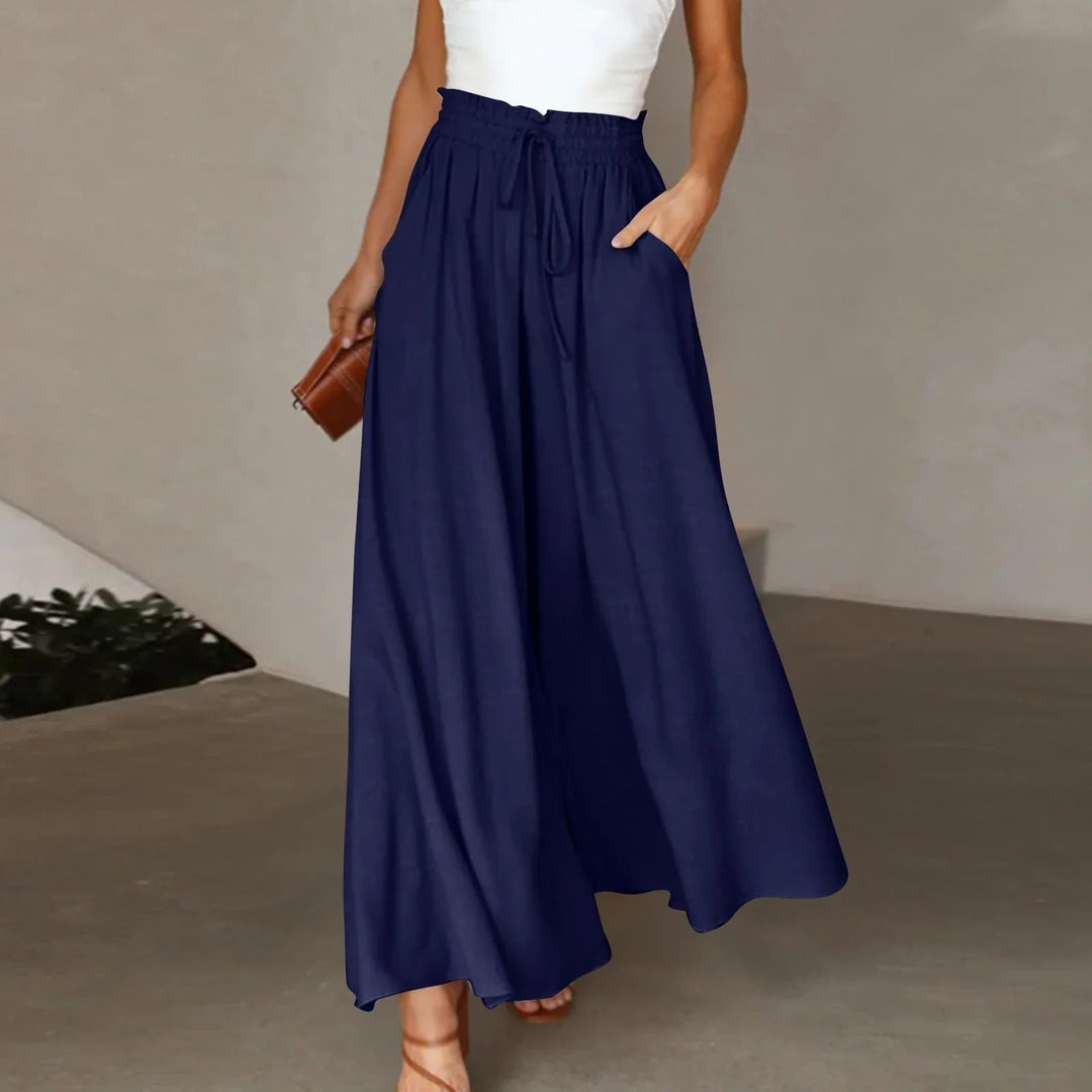 Woman wearing navy high-waisted wide leg pants with drawstring and pockets, holding brown clutch