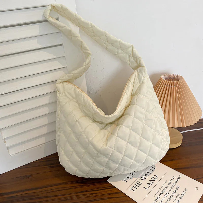 Cream quilted shoulder bag on wooden table with folded lamp and book titled The Waste Land
