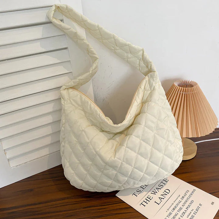 Cream quilted shoulder bag on wooden table with folded lamp and book titled The Waste Land