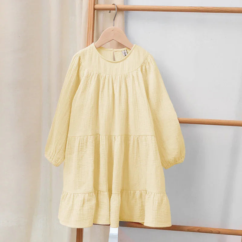 Light yellow long-sleeve toddler dress with ruffle hem hanging on wooden hanger