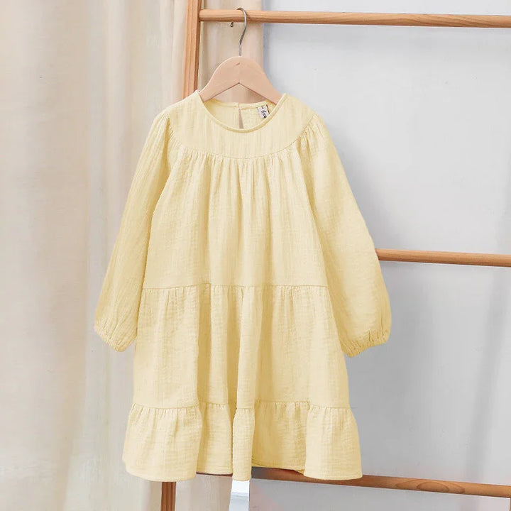 Light yellow long-sleeve toddler dress with ruffle hem hanging on wooden hanger