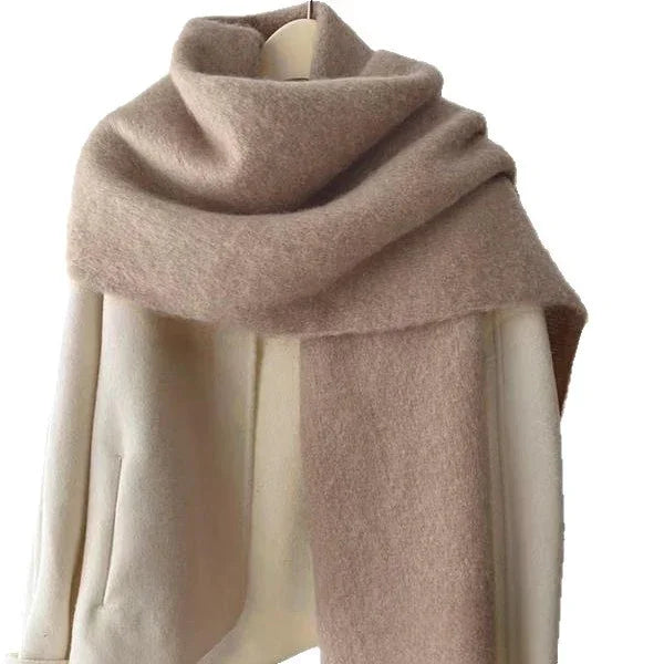 beige woolen scarf draped over cream coat on hanger against white background