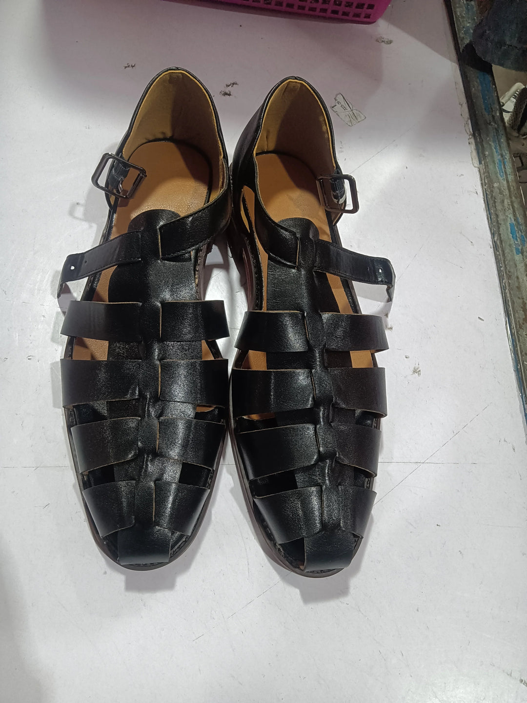 Pair of black leather woven sandals with buckles on white surface