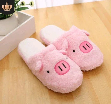 Soft pink pig-themed plush slippers on wooden floor with potted plant in background
