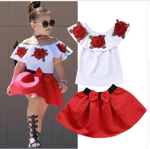 Toddler girl wearing white off-shoulder top with red embroidered roses and red skirt with bow, summer outfit
