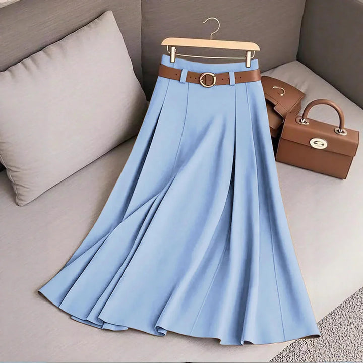 Light blue pleated midi skirt with brown belt on hanger, placed on beige couch with brown handbags