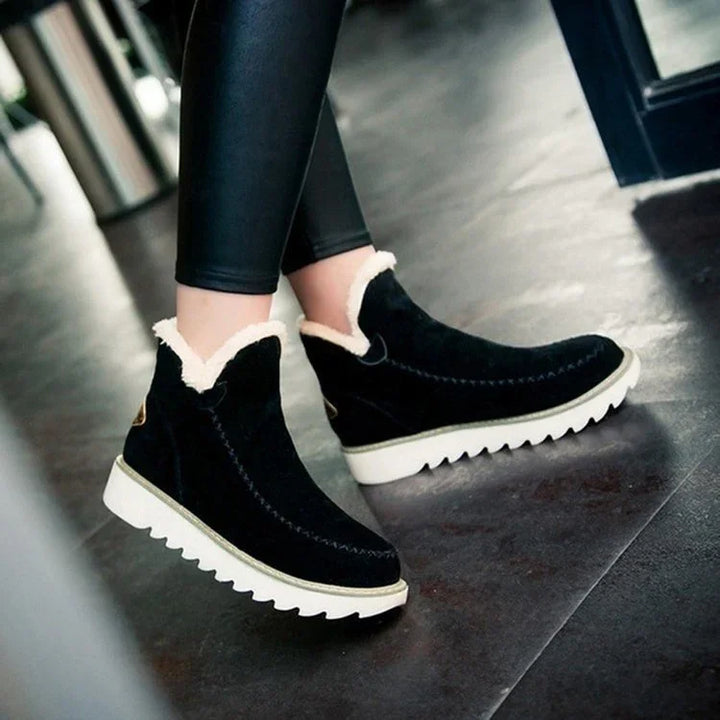Black suede ankle boots with white faux fur lining and thick white soles worn with black leggings on indoor floor