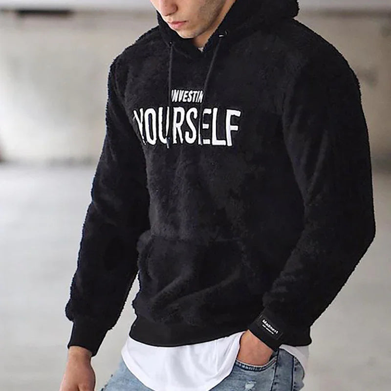 Man wearing black fuzzy hoodie with white text 'INVESTIN YOURSELF' in casual indoor setting