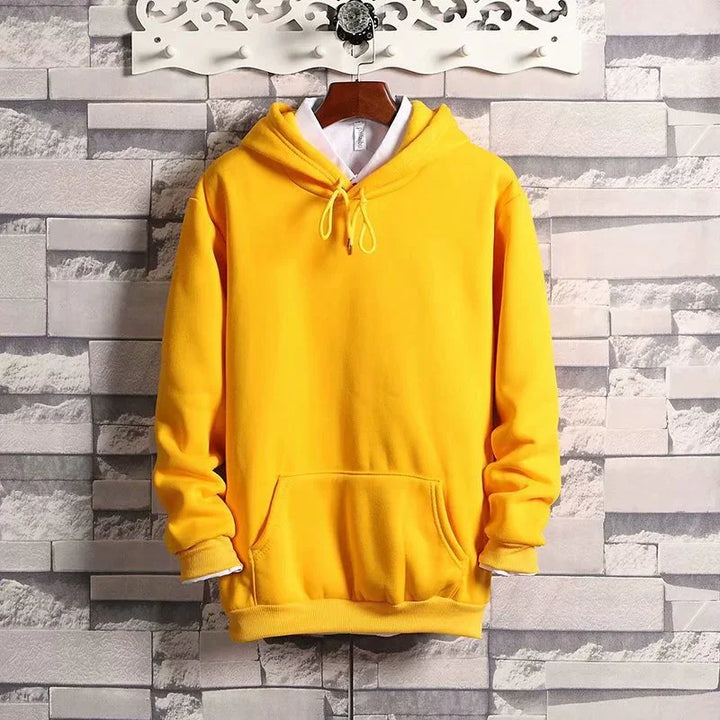 Bright yellow hoodie with front pocket and drawstring hood on wooden hanger against gray stone wall
