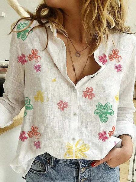 White linen button-up blouse with colorful floral prints worn with blue jeans in casual indoor setting