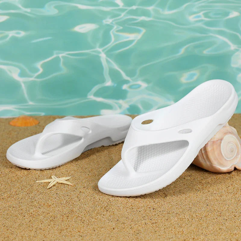 White beach sandals on sandy shore with seashell and starfish near clear pool water