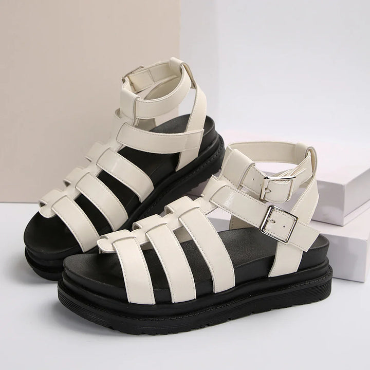 White strappy buckle sandals with thick black soles on a white and beige background