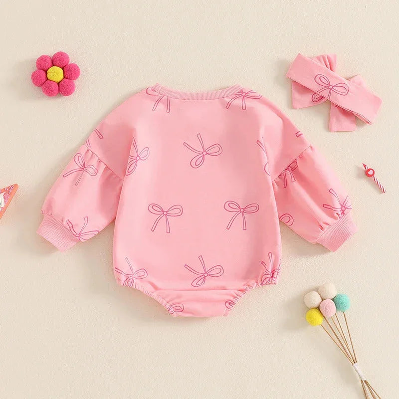 Pink baby romper with long sleeves and bow patterns, paired with a matching pink bow headband