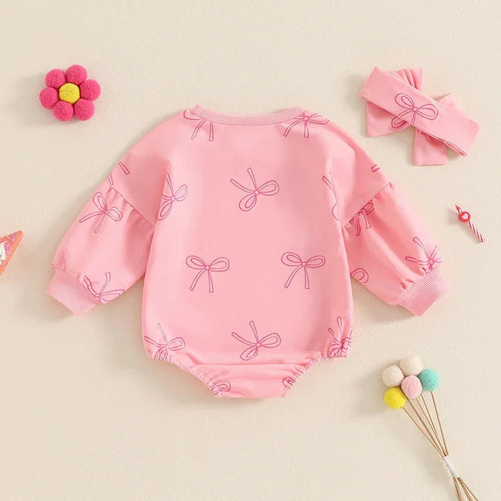 Pink baby romper with long sleeves and bow patterns, paired with a matching pink bow headband