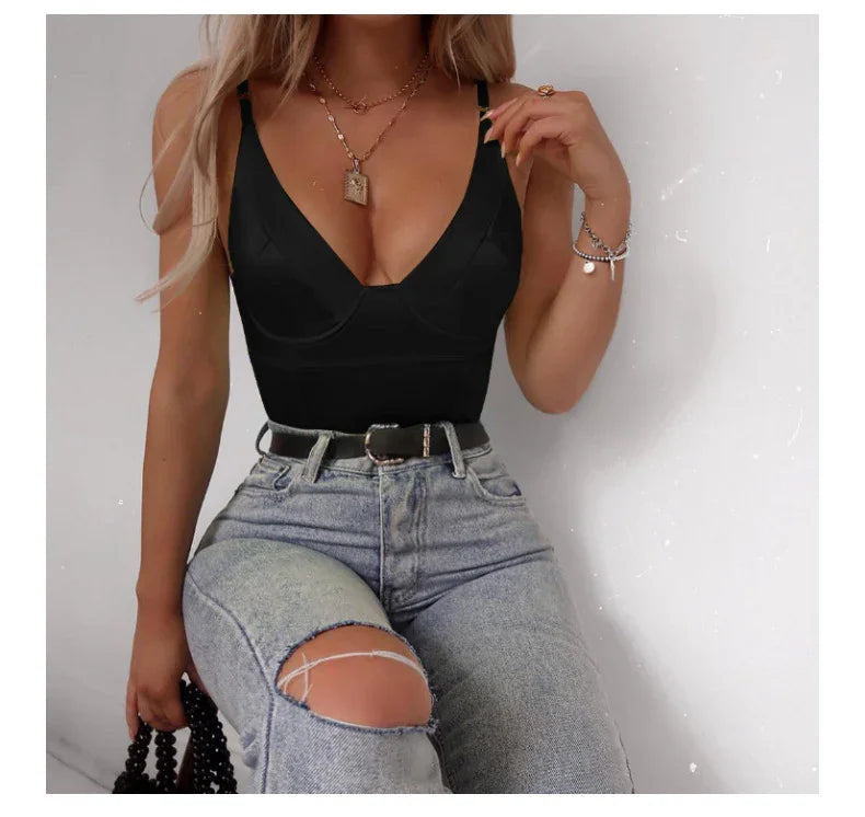 Woman wearing black fitted tank top and ripped light wash jeans sitting against white wall