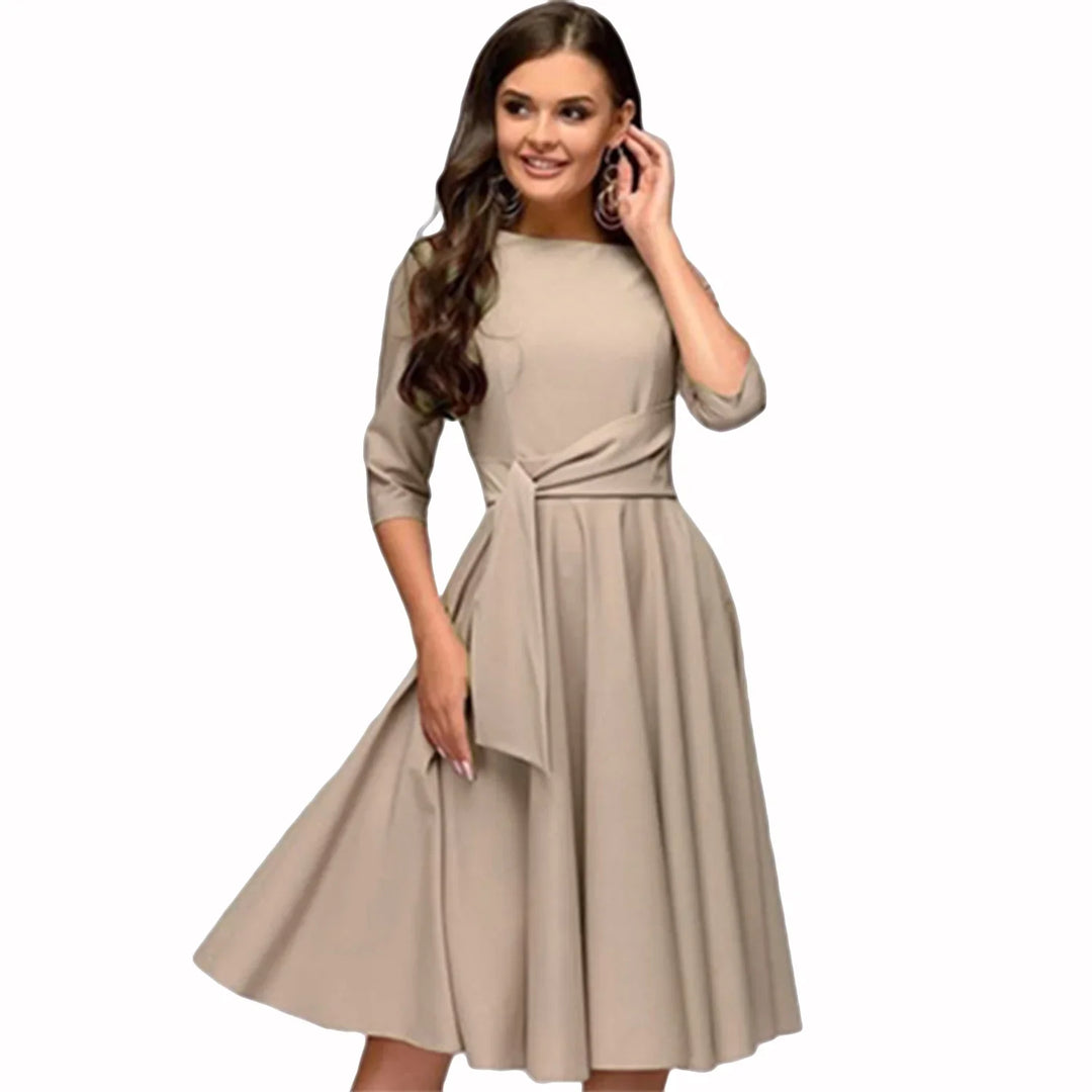 Woman in beige midi dress with half sleeves and tied waist bow, smiling and posing