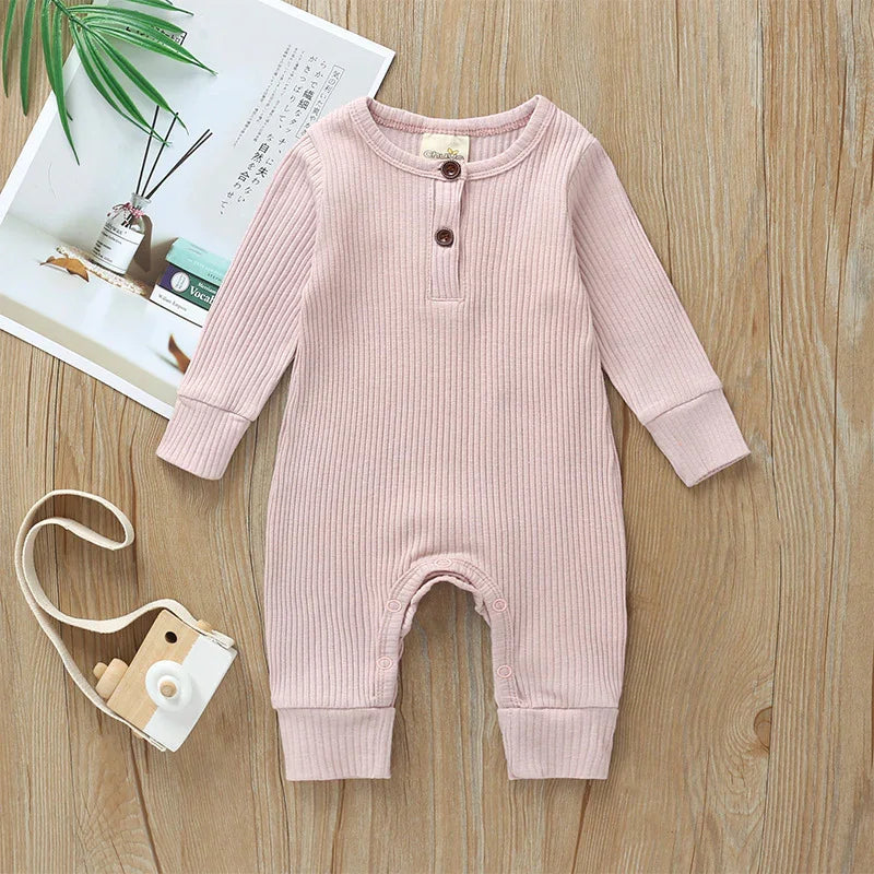 Soft pink ribbed baby romper with long sleeves and buttons, displayed on wooden surface