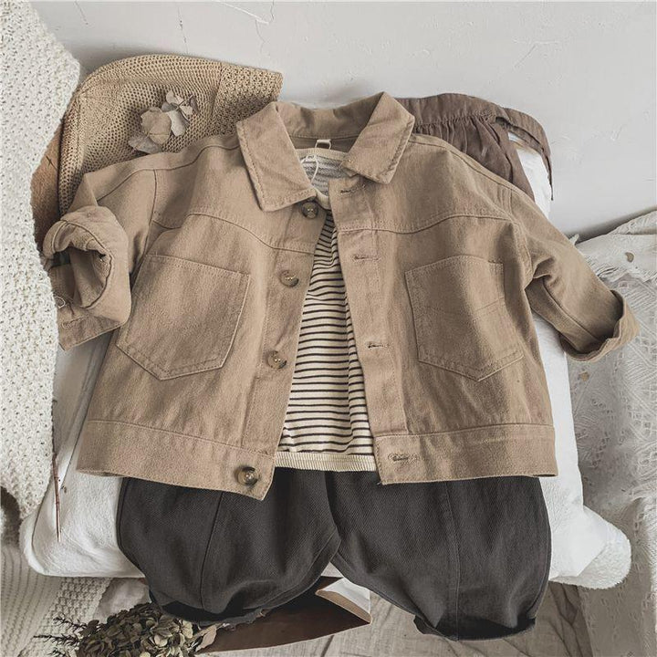 Casual kid's outfit with tan jacket, striped shirt, and black pants laid on knit and lace textiles