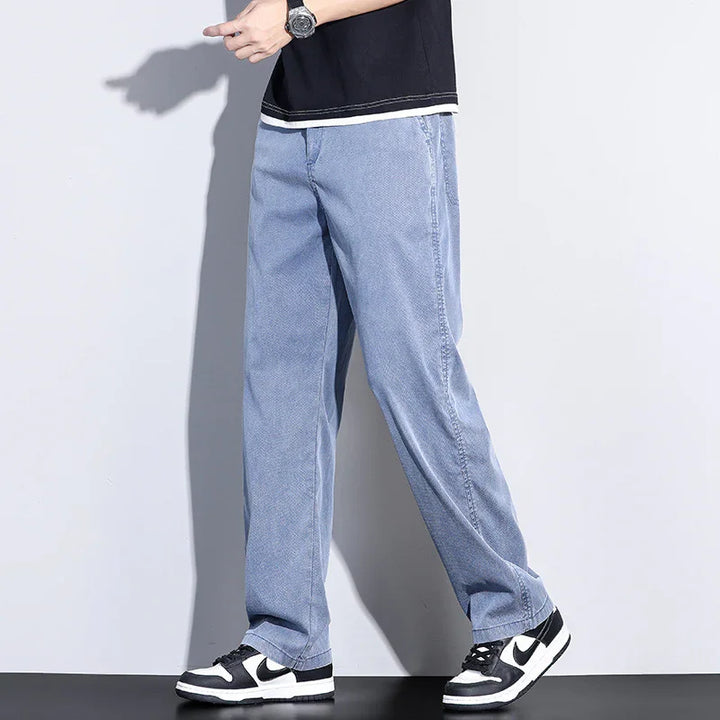Man wearing light blue baggy jeans with black and white sneakers against plain background