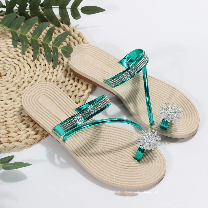 Beige sole sandals with shiny turquoise straps and rhinestone flower toe decorations on a white surface