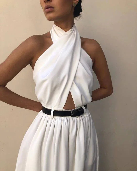 Woman wearing white sleeveless crisscross halter dress with black belt against plain background