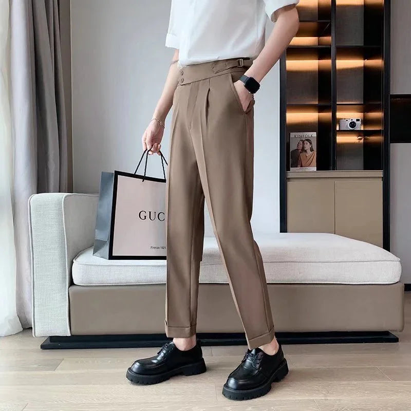 Person wearing brown tailored trousers and black shoes holding a Gucci shopping bag indoors