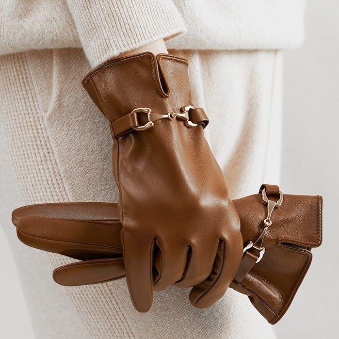 Close-up of hands wearing and holding brown leather gloves with gold hardware on beige knitwear background