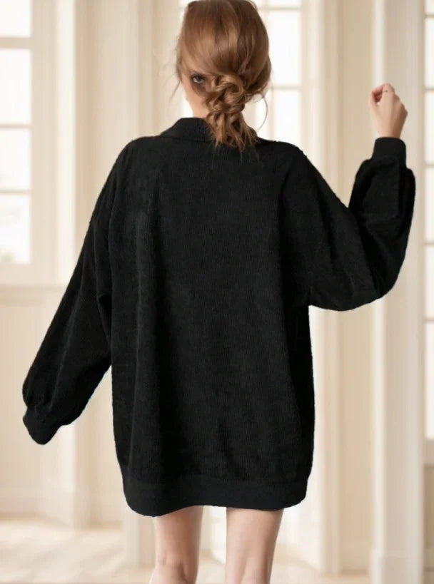 Woman seen from back wearing oversized black sweater in bright room with large windows