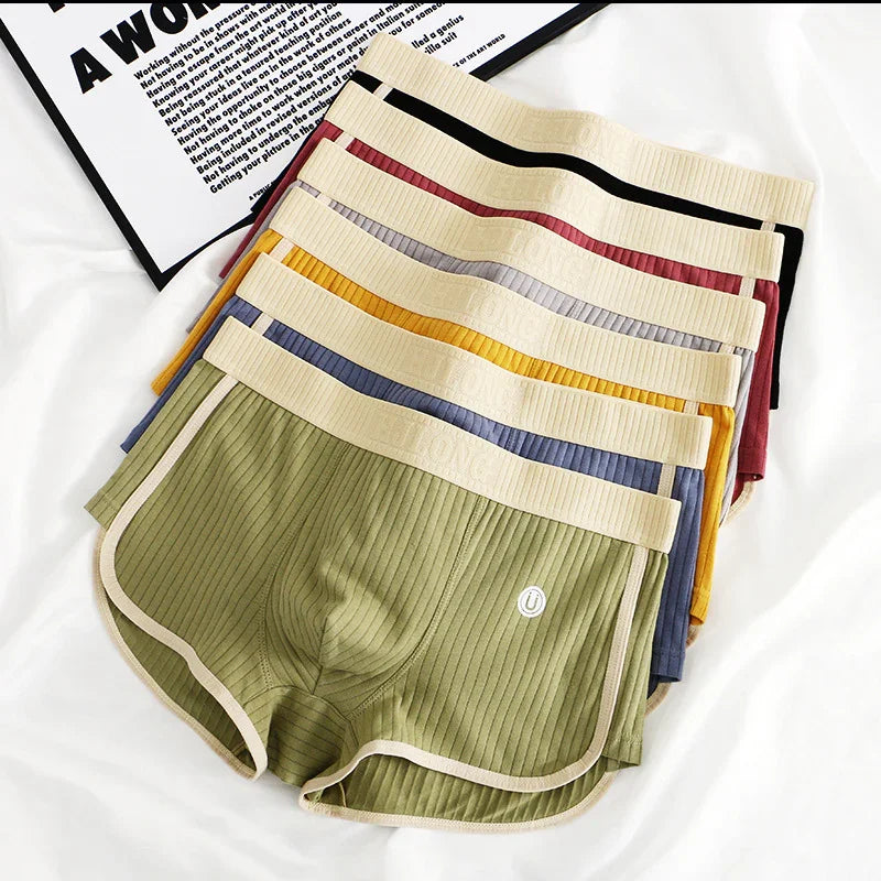 Stack of ribbed fabric men's boxer briefs in green, blue, yellow, gray, red, and black with beige elastic waistbands on white background
