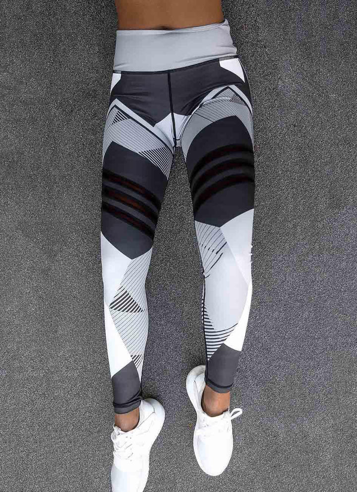 Woman wearing black, white, and gray geometric patterned high-waist workout leggings with white sneakers on asphalt